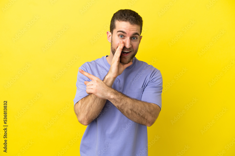 Handsome blonde man over isolated yellow background pointing to the side to present a product and whispering something Handsome blonde man over isolated yellow background pointing to the side to present a product and whispering something