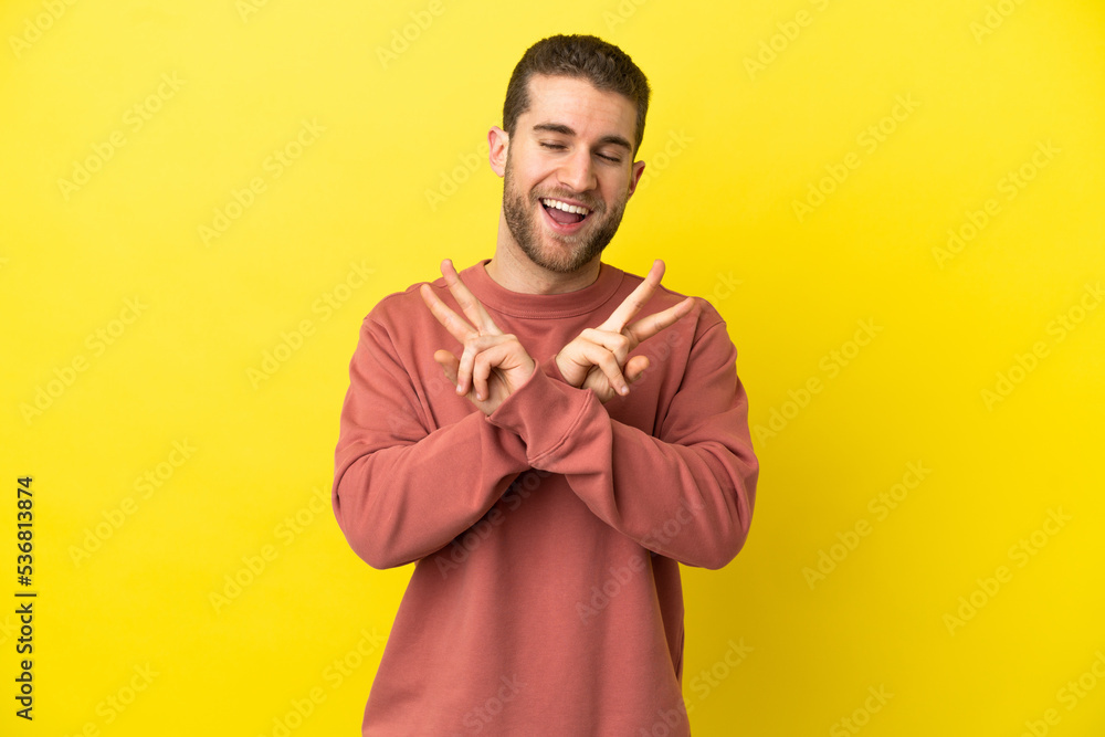Handsome blonde man over isolated yellow background smiling and showing victory sign Handsome blonde man over isolated yellow background smiling and showing victory sign