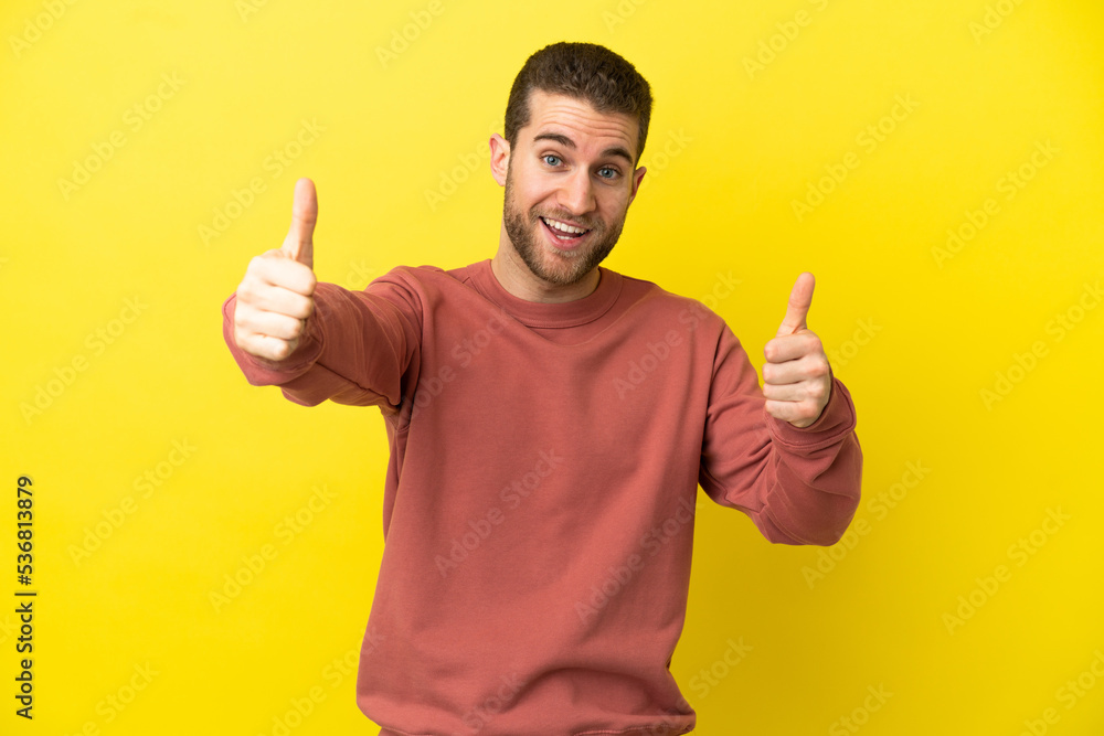 Handsome blonde man over isolated yellow background giving a thumbs up gesture