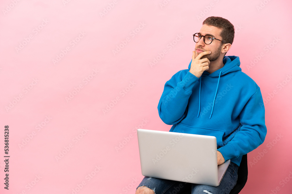 Young man sitting on a chair with laptop having doubts and with confuse face expression Young man sitting on a chair with laptop having doubts and with confuse face expression