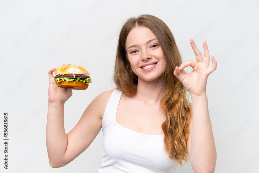 Young pretty woman holding a burger isolated on white background showing ok sign with fingers