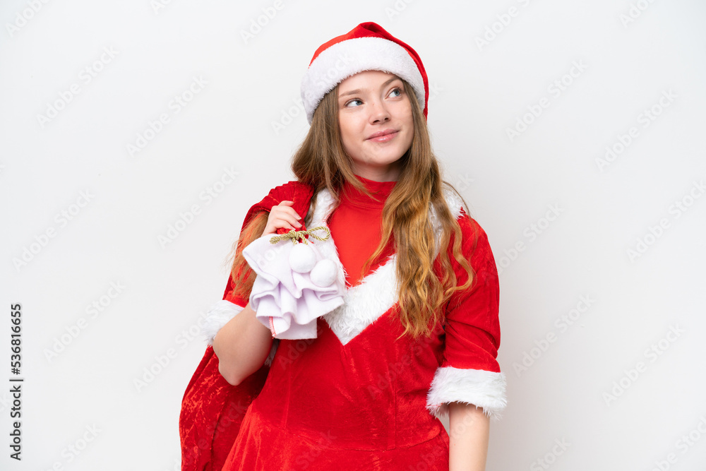 Young caucasian woman with Christmas dress holding Christmas sack isolated on white background looking up while smiling Young caucasian woman with Christmas dress holding Christmas sack isolated on white background looking up while smiling