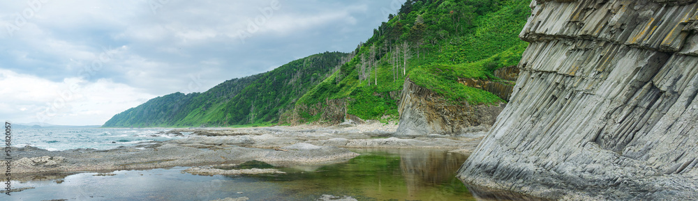 coastal landscape, panorama with beautiful columnar basalt cliff on the wooded coast of Kunashir island coastal landscape, panorama with beautiful columnar basalt cliff on the wooded coast of Kunashir island