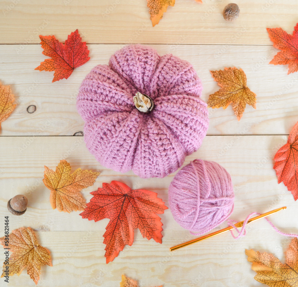 woolen crochet pumpkins on wooden ground, with crochet hooks and autumn leaves