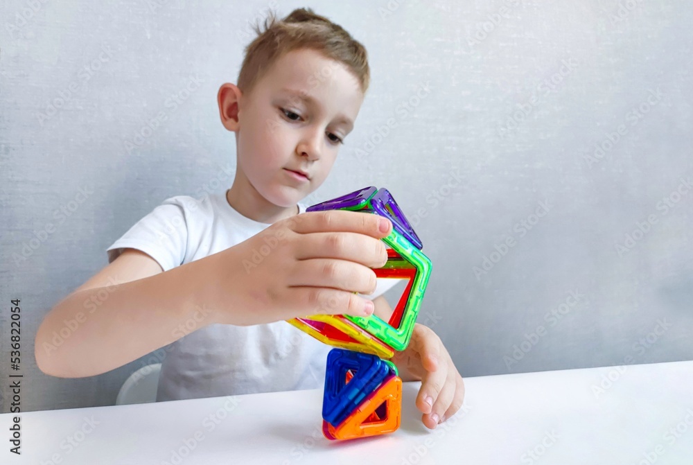 a child plays with a magnetic constructor on a white table. Game with a magnetic constructor for development a child plays with a magnetic constructor on a white table. Game with a magnetic constructor for development