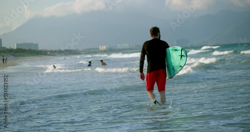 A retired athlete enters the sea, goes to ride on the waves on surfing dos. Portrait of a handsome senior sportsman at the age carrying a surfboard on the beach.