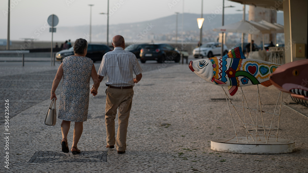 Φωτογραφία casal idoso de costas a passear de mãos dadas numa urbe costeira ao fim da tarde