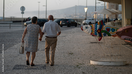 casal idoso de costas a passear de mãos dadas numa urbe costeira ao fim da tarde photo