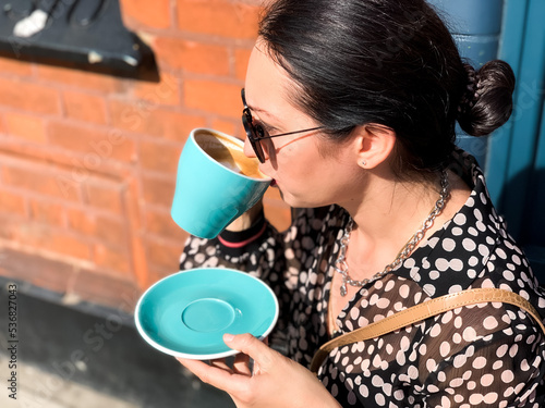 Young candid woman drinking morning coffee in tiffany color ceramic mug with saucer on cafe terrace.