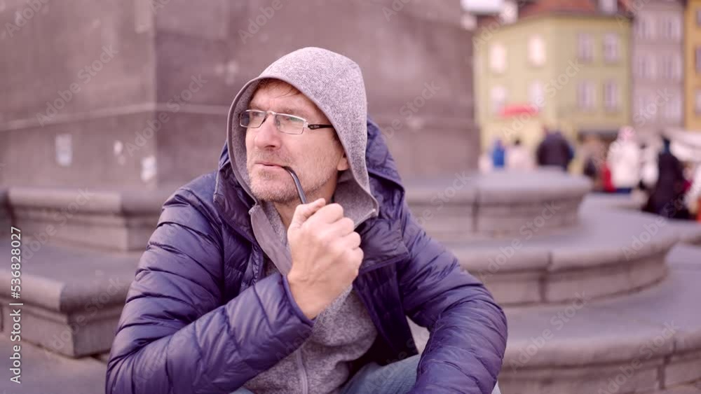 Close-up of adult man sitting in the hood on square and smoking a tobacco pipe in the Palace Square, Warsaw Old Town
Close-up of adult man sitting in the hood on square and smoking a tobacco pipe in the Palace Square, Warsaw Old Town
