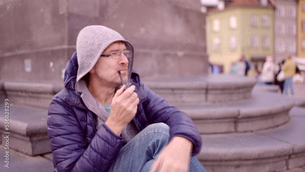 Close-up of adult man sitting in the hood on square and smoking a tobacco pipe in the Palace Square, Warsaw Old Town
Close-up of adult man sitting in the hood on square and smoking a tobacco pipe in the Palace Square, Warsaw Old Town
