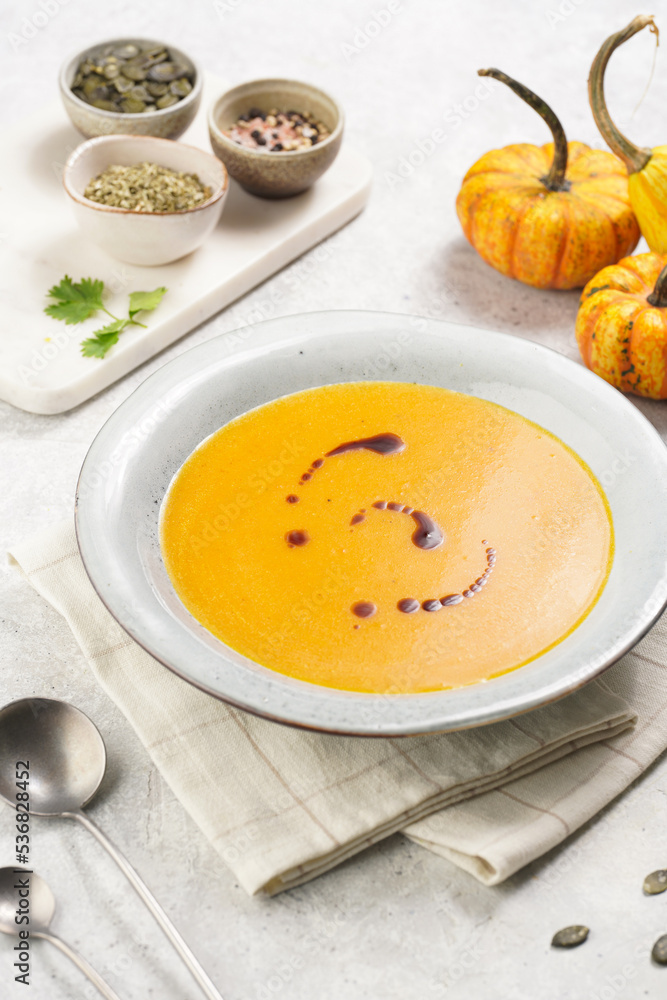 One deep grey soup bowl with an orange pumpkin cream soup with pumpkin seed oil, on a gray concrete background One deep grey soup bowl with an orange pumpkin cream soup with pumpkin seed oil, on a gray concrete background
