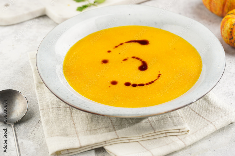 One deep grey soup bowl with an orange pumpkin cream soup with pumpkin seed oil, on a gray concrete background One deep grey soup bowl with an orange pumpkin cream soup with pumpkin seed oil, on a gray concrete background