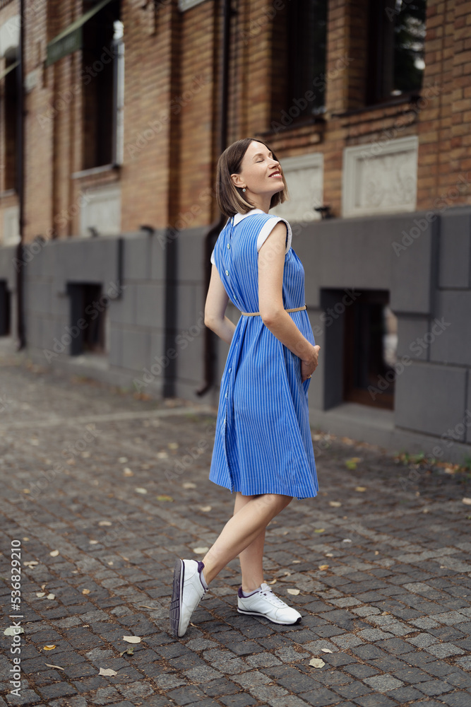 Fototapeta premium Happy pregnant woman chilling and having fun while walking in the city in a midi blue vintage dress. Happiness all around