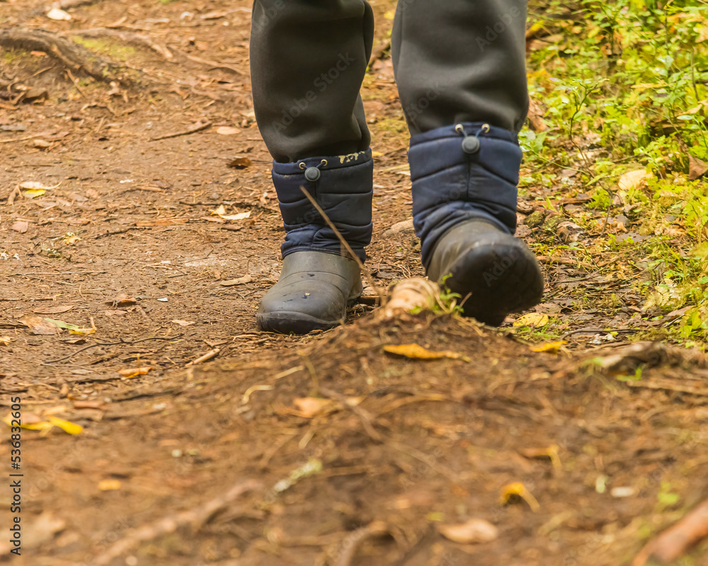 the legs of an adult dressed in warm old boots for traveling, walking through a green forest. the legs of an adult dressed in warm old boots for traveling, walking through a green forest.