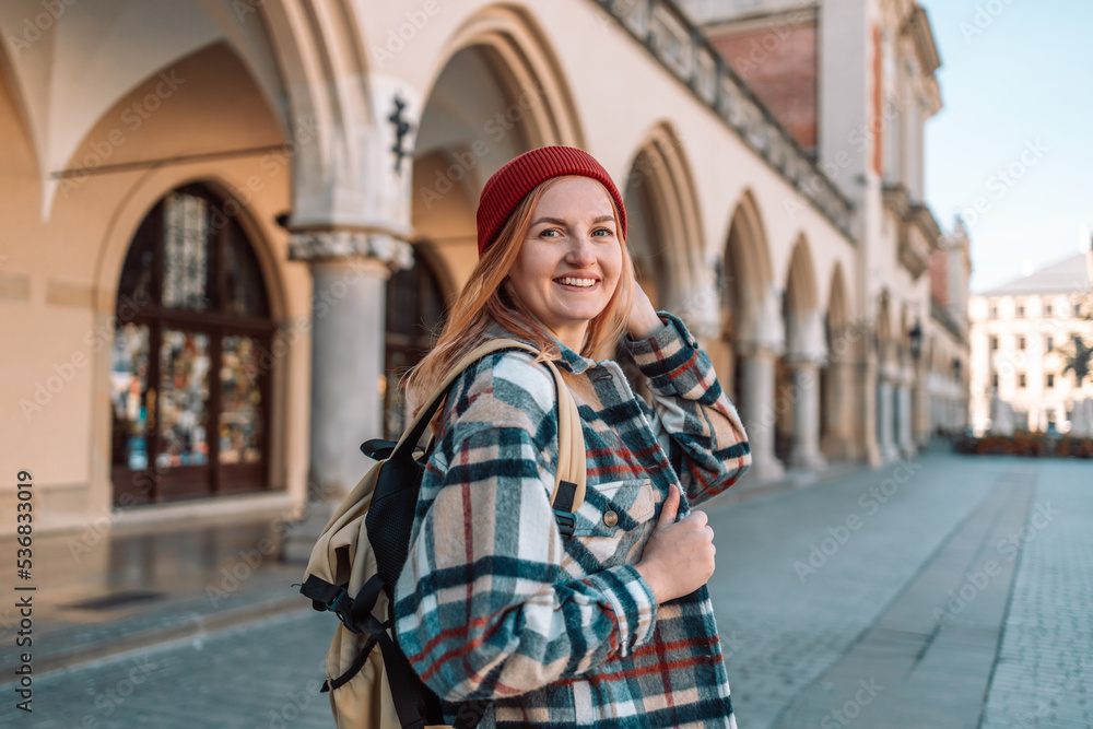 Obraz premium Rear view of 30s traveler woman carrying backpack on her shoulders visiting old city of Krakow, active lady enjoying travel and discovery.