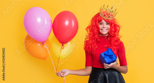 smiling child in crown with gift box and party balloon on yellow background