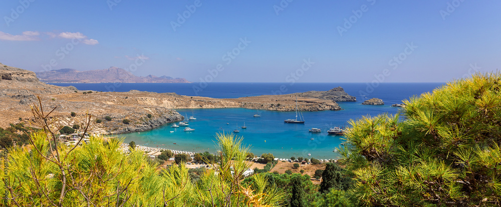 Panoramic view of colorful harbor in Lindos village and Acropolis, Rhodes. Aerial view of beautiful landscape, ancient ruins, sea with sailboats and coastline of island of Rhodes in Aegean Sea