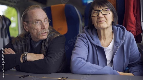 Elderly couple is riding in a train carriage and looking out the window and talking with each other   photo