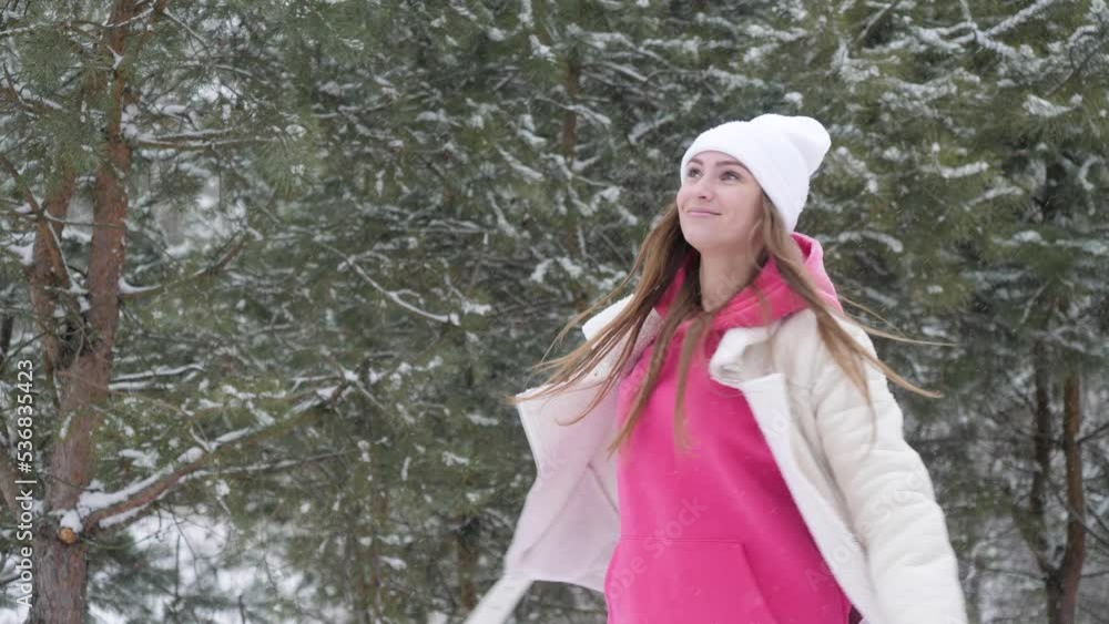 Young beautiful brunette woman with long hair in white and pink clothes is spinning with her arms outstretched to the sides in winter in snowy forest Young beautiful brunette woman with long hair in white and pink clothes is spinning with her arms outstretched to the sides in winter in snowy forest