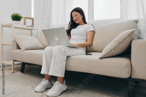 Asian woman sits with laptop and phone in home freelancer's hangout with staring at laptop screen working, lifestyle work and home