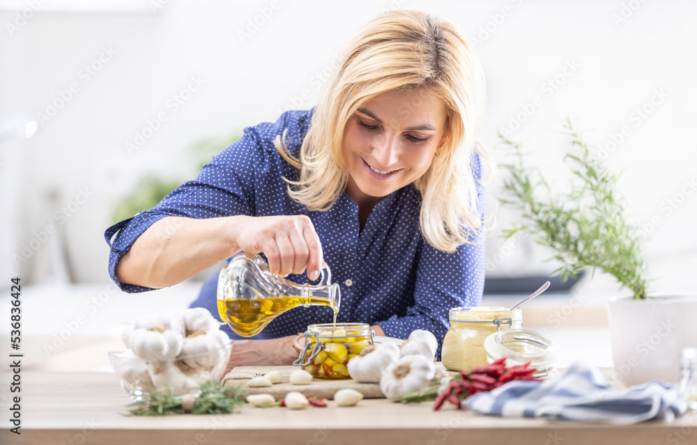 Blonde woman pours oil over garlic cloves peeled in a jar, making preserved for winter time