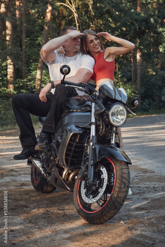 Young beautiful couple talking and having fun  sitting on a motorcycle  traveling together on a forest road