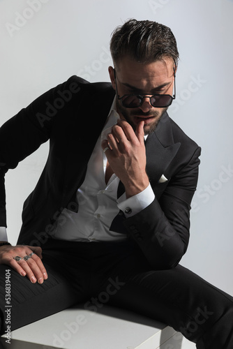 sensual groom in black tuxedo touching lips and looking down © Viorel Sima