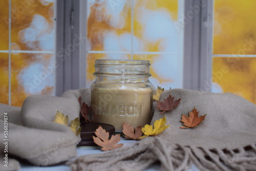 Mason jar scented candle with beige scarf and Fall leaves. 