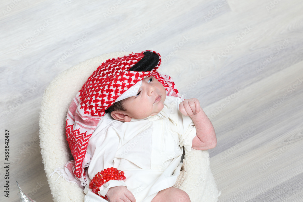 Saudi Muslim 1 month newborn boy in traditional arabian dressing white thobe red shemagh black agal Stock Adobe Stock