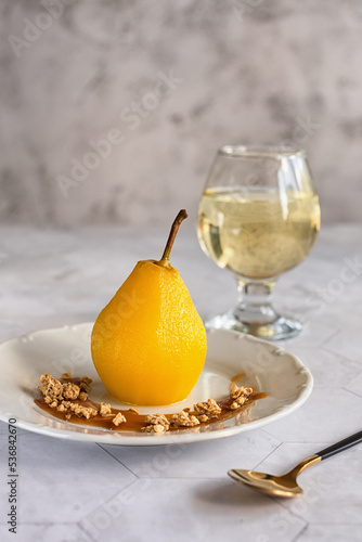 Delicious homemade autumn dessert: pears boiled in white wine. Pears in white wine with caramel and a glass of white wine on a light marble table. Light fruit dessert. photo