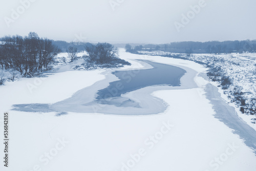 View from a height of a frozen river covered with snow. Cold winter. Beautiful ice patterns on the river from above