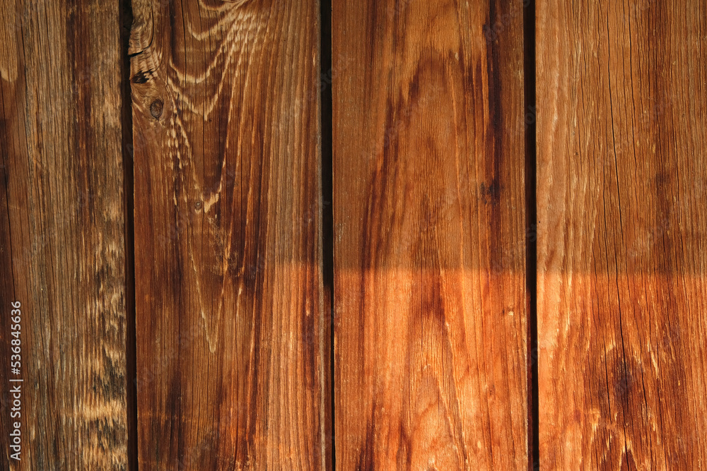 Obraz premium The texture of an old fence with a shadow. Wood texture with vertical lines. The texture of wood with knots and holes. The background of a fence damaged by time.