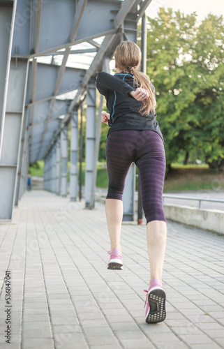 Young athletic woman warming up and running along the path, fitness outdoor