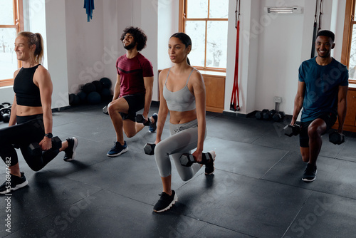 Group of multiracial young adults doing lunges with weights at the gym