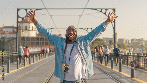 Obraz na plátně Happy Young african american traveller man with cmera on the Dom Luis Bridge, Porto