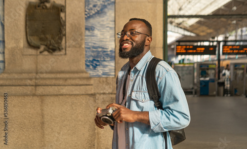 Smiling african american man with cmera at european terminal train station. Tourist travel by train on vacation time holiday weekend trip. photo