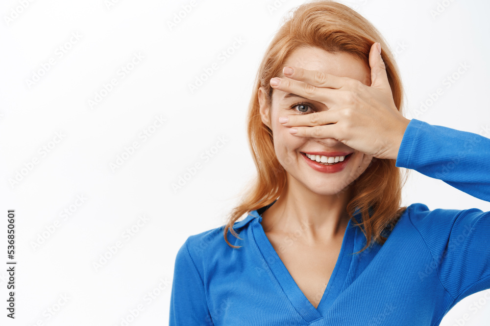 Close up portrait of smiling happy woman covers her eyes, peeks through fingers, intrigued by surprise, stands over white background Close up portrait of smiling happy woman covers her eyes, peeks through fingers, intrigued by surprise, stands over white background