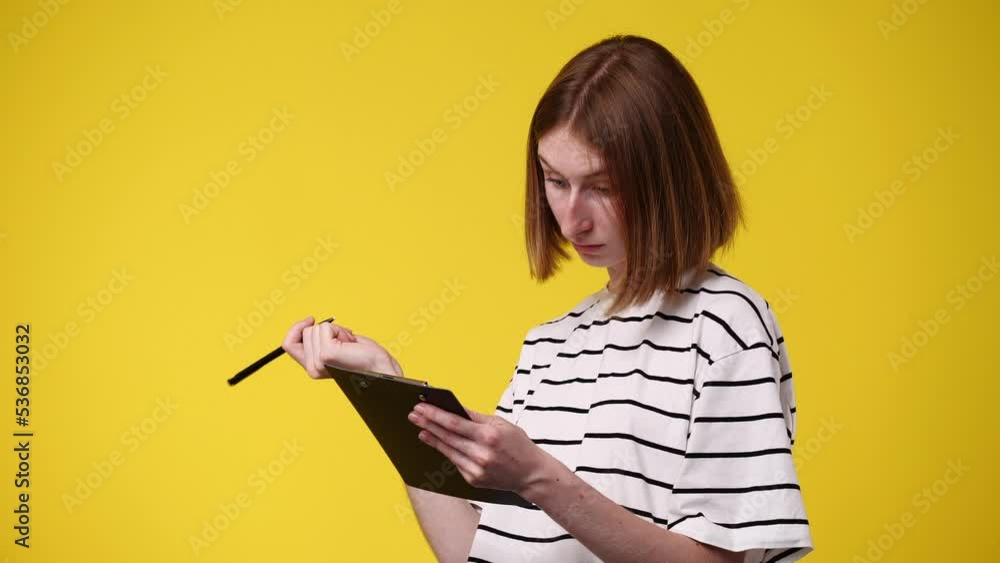 4k video of concentrated woman writing down something isolated over yellow background. 4k video of concentrated woman writing down something isolated over yellow background.