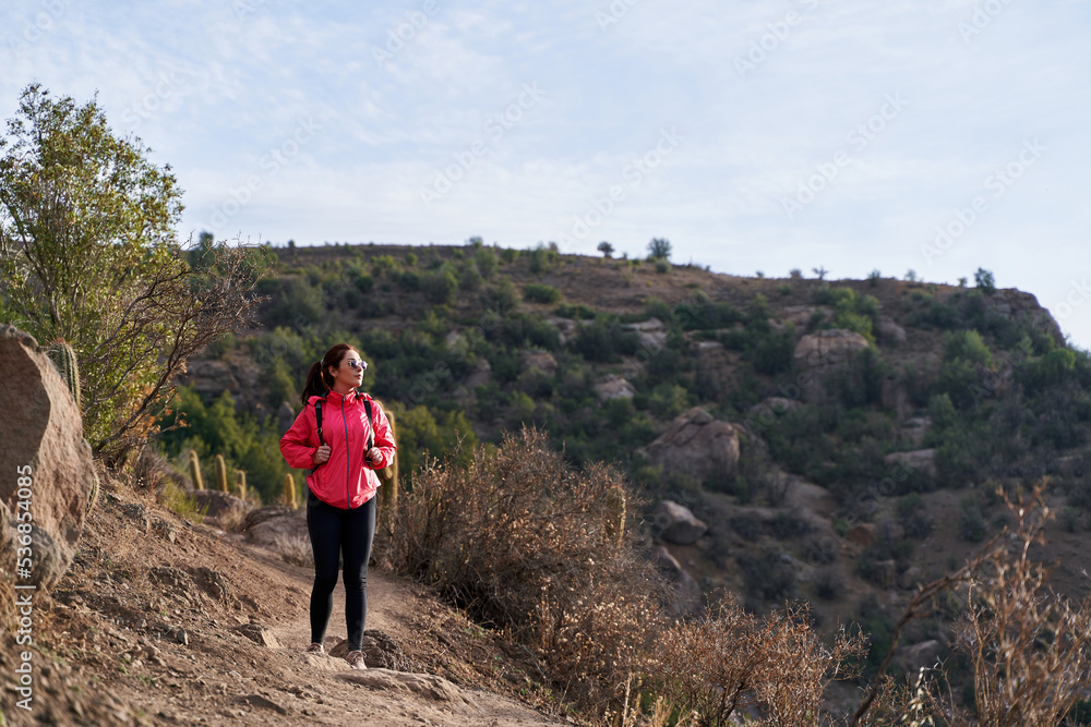 young woman with red jacket and backpack, descending the mountain in the middle of the Andes Mountains of Chile young woman with red jacket and backpack, descending the mountain in the middle of the Andes Mountains of Chile