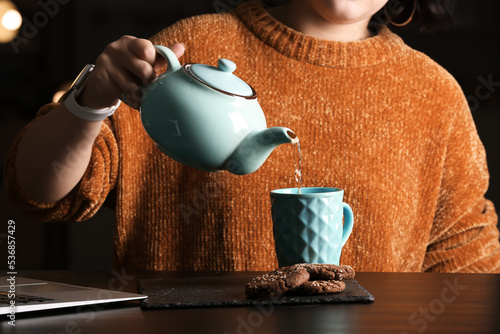 Принти на полотні Woman pouring tea into cup at table in cafe, closeup