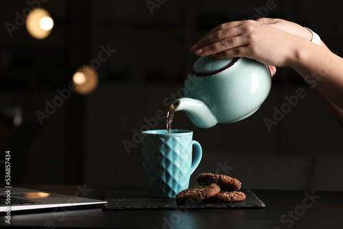 Woman pouring tea into cup at table in cafe