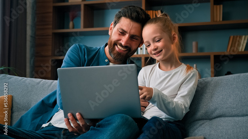 Fotografie Cheerful father and little beautiful daughter girl sit on couch watch movies car