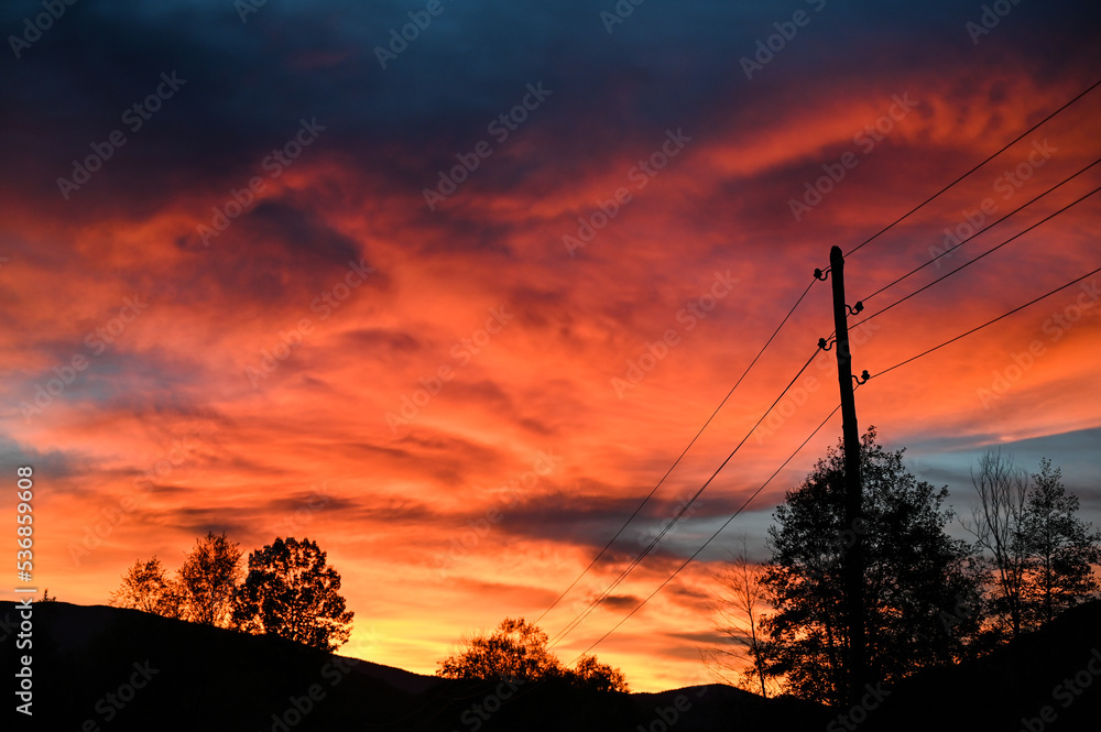 Beautiful orange sunset in summer. Electric poles with power lines at sunset. Electricity transmission.