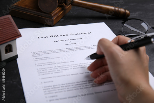 Woman signing last will and testament at black table, closeup photo