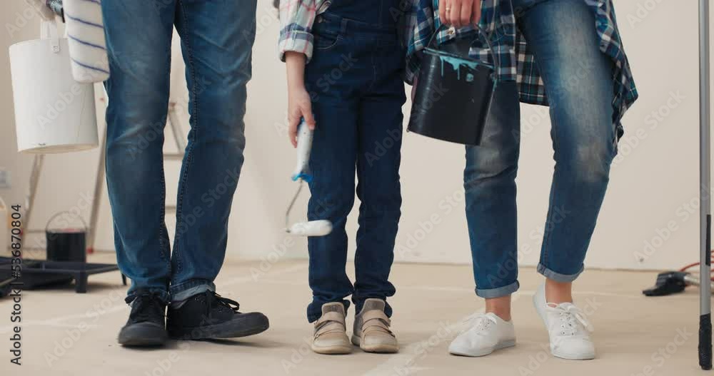 Close-up of legs of girl and parents. They are holding rollers and buckets of paint, wearing jeans, shirts and sneakers. Happy family having fun and dancing. They are ready to paint walls in new house Close-up of legs of girl and parents. They are holding rollers and buckets of paint, wearing jeans, shirts and sneakers. Happy family having fun and dancing. They are ready to paint walls in new house