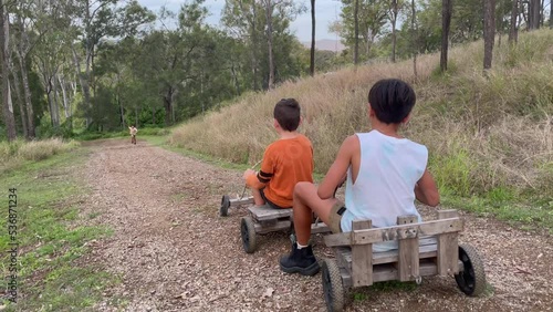 Excited kids dare to ride old-fashioned wooden go karts down a steep dirt road photo