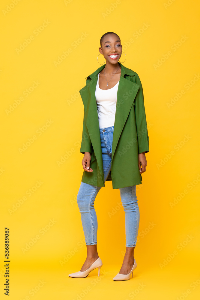 Fototapeta premium Full length portrait of trendy fashionable African American woman standing in yellow color studio isolated background