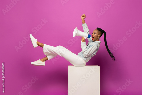 Young African American woman shouting on megaphone and raising fist in studio purple pink color isolated background photo