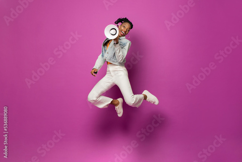 Billede på lærred Energetic trendy young African American woman jumping with megaphone in studio p